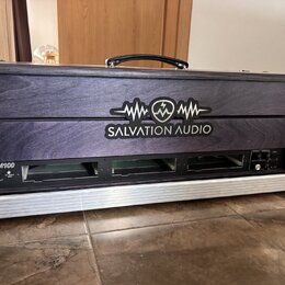Černý transportní kufřík s dřevěným předním panelem a hliníkovým rámem. Na panelu je bílé logo s nápisem SALVATION AUDIO a grafickým symbolem vlny. V…