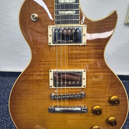 Elektrická kytara s trupem z plaménovky v žlutohnědém gradientu. Nástroj má dva humbuckery s krémovými rámečky, Tune-o-matic kobylku a stopbar struno…