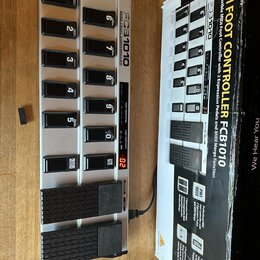 Stříbrný MIDI kontrolér s černými spínači a dvěma expresními pedály. Na přístroji je nápis FCB1010 MIDI FOOT CONTROLLER a na pedálech logo Behringer.…