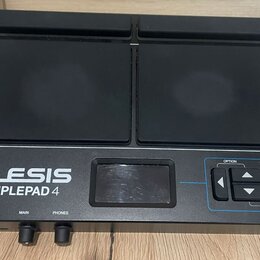 Černý elektronický samplepad s dvěma velkými gumovými pady. Na přístroji je bílý nápis ALESIS SAMPLEPAD 4 a v pravé části ovládací prvky s popisky OP…