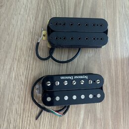Dva elektrické kytarové snímače typu humbucker v černé barvě. Horní snímač má černé plastové krytky s viditelnými poloslnoidy. Dolní snímač má stříbr…