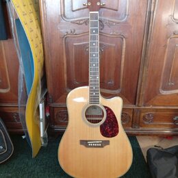Akustická kytara s cutawayem v přirozené dřevěné barvě a červeným puntovaným pickguardem. Na hlavě hmatníku je viditelné logo Epiphone. Hmatník obsah…