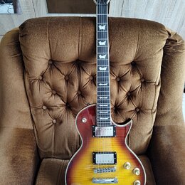 Elektrická kytara s trupem v žlutě-červené barvě sunburst a hnědým hmatníkem. Na hlavě je bílý nápis BACH a logo ve tvaru stylizovaného písmene E. Ná…
