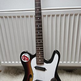 Elektrická kytara s trupem v sunburst provedení a bílým pickguardem. Na hlavě hmatníku je nápis Squier STRAT a logo Fender. Trup vykazuje výrazné opo…