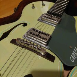 Světle zelená polodubová elektrická kytara s tmavě zeleným plechtrátorem. Na plechtrátoru je viditelný bílý nápis GRETSCH. Nástroj má dva snímače s k…
