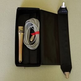 Černý úzký kufr, ve kterém je umístěn stříbrný mikrofon a srolovaný šedý kabel. Kabel je svázaný červeným plastovým stahovákem. V pravé části je přip…