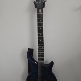 Elektrická kytara s tmavě modrým trupem s výraznou strukturou dřeva a černým hmatníkem. Na hlavě je bílý nápis Sterling by Music Man. Nástroj má dva…
