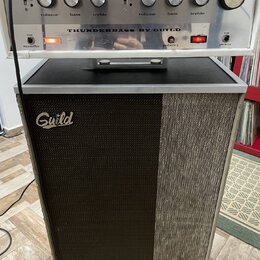Kytarový zesilovač s hlavou umístěnou na samostatném boxu. Na předním panelu hlavy je nápis THUNDERBASS BY GUILD a ovládací prvky s popisky volume, b…