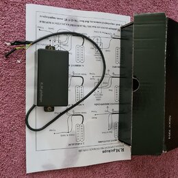 Černý plastový box s elektronikou a připojenými vodiči, položený na papírovém návodu k zapojení. Na boku boxu je bílý nápis R.M.pickups. Vedle zaříze…