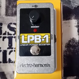 Kytarový efekt v stříbrném kovovém krytu umístěný na žluté krabici. Na zařízení je černý panel s nápisy „LPB-1“, „LINEAR POWER BOOSTER“ a „BOOST“, če…