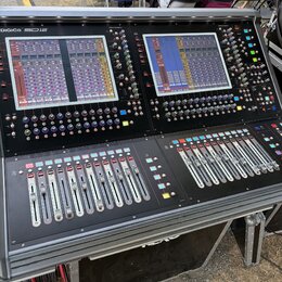 Černý digitální mixovací pult s dvěma velkými barevnými displeji a řadami posuvníků. V levém horním rohu je bílý nápis DiGiCo SD12. Povrch obsahuje m…