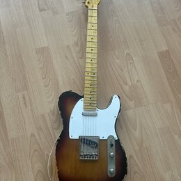 Elektrická kytara typu Telecaster s javorovým hnedým krčkem a korpusem v tmavě hnědém sunburst provedení. Na hlavě krku je viditelné logo Fender. Bíl…