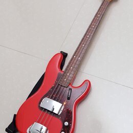 Čtyřstrunná elektrická basová kytara s červeným trupem a hnědým hmatníkem. Na korunce je viditelné logo Squier. Kytara má tmavě hnědý pickguard s tex…