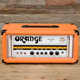 Kytarový kombozesilovač v oranžovém vinylu s černými rohy a úchytem. Na předním panelu je velký nápis ORANGE a označení modelu ROCKER 30. Ovládací pa…