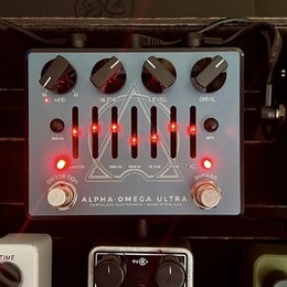 Stříbrný efekt pedál s nápisy ALPHA OMEGA ULTRA a DARKGLASS ELECTRONICS - MADE IN FINLAND. Na horní straně jsou čtyři černé ovládací knoflíky s popis…