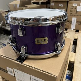 Fialový buben s chromovaným obručováním a kování, umístěný na kartónovém krabici. Na korpusu je zlatý štítek s nápisy „S.L.P.“, „SOUND LAB PROJECT“ a…