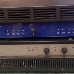 Dva rackové výkonové zesilovače naskládané na sebe. Horní zařízení je modré s černým horním krytem a nápisy PROFESSIONAL POWER AMPLIFIER, logo AG aku…