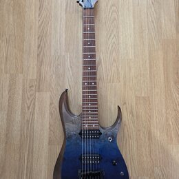Elektrická kytara s modrým přechodovým lakem a viditnou strukturou dřeva na hranách. Na hlavě hmatníku je bílý nápis Ibanez. Nástroj má dva humbucker…