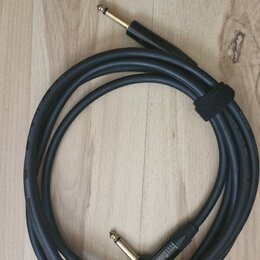 Černý instrumentální kabel s pozlacenými konektory typu jack. Na povrchu kabelu je bílý nápis GUITAR INSTRUMENT CABLE. Kabel je svázaný černým suchým…