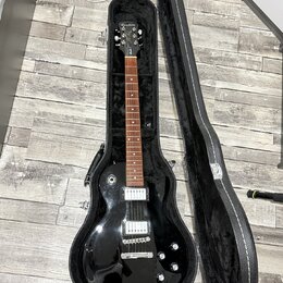 Černá elektrická kytara v otevřeném černém tvrdém pouzdře. Na hlavě hmatníku je bílý nápis Epiphone. Nástroj má dva humbuckery, čtyři ovládací knoflí…