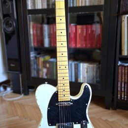 Elektrická kytara typu Telecaster v krémové barvě se světlým hnedem dřevěného krku a hmatníkem. Na hlavě je viditelné logo "Telecaster". Tělo vykazuj…
