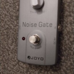 Stříbrný efekt pedál s nápisem Noise Gate a logem JOYO. Na horní části je bílý ovládací knoflík s popiskem Threshold a ve spodní části stříbrný spína…