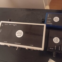 Sada bezdrátového systému tvořící tři černé a modré komponenty. Na všech třech je bílý kulatý štítek s nápisem ROCKY WIRELESS SYSTEM. Největší jednot…