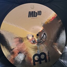 Kulatý mosazný činel s kladivkovaným povrchem. Na horní části je černý nápis Mb10 a pod ním text 16" Medium Crash, v horní části je viditelné logo ME…