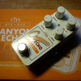 Bílý efekt pedál s nápisy ehx, Canyon ECHO a NYC DSP. Na horní straně se nachází pět bílých oválných knoflíků s popisky FILTER, BLEND, TAPE DIV, FDBK…