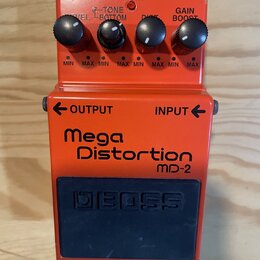 Kytarový efekt pedál oranžové barvy s modrým spínacím tlačítkem. Na přední straně je nápis Mega Distortion MD-2 a na spínači vyražené logo BOSS. V ho…