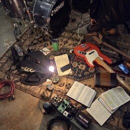Fotografie zachycuje hudební vybavení rozložené na vzorném koberci. Je zde vidět bicí souprava s nápisem SONOR na basovém bubně, červená elektrická b…
