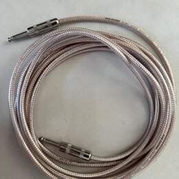 Stříbrný pletený instrumentální kabel s dvěma 6,3mm jack konektory. Konektory mají kovové stínění s drážkovaným povrchem. Na kabelu jsou viditelné ne…