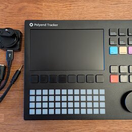 Černý sampler Polyend Tracker s displejem, mřížkou bílých podsvícených polí a ovládacím knoflíkem. Na horní hraně je bílý nápis Polyend Tracker s log…