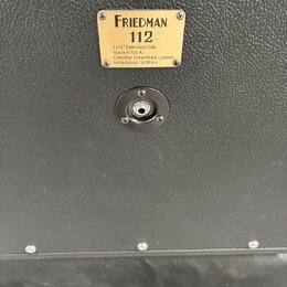 Detail zadní strany černého kytarového boxu s texturovaným povrchem. Na zlatém štítku je nápis FRIEDMAN 112, pod ním text 1x12" Extension Cab, Made i…