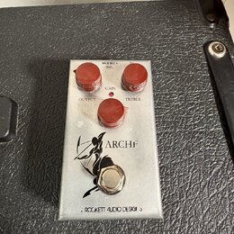 Kovový efekt pedál stříbrné barvy s třemi červenými oválnými knoflíky. Na horní části jsou nápisy MADE IN USA, 9VDC, GAIN, OUTPUT a TREBLE. Uprostřed…