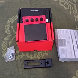 Červený elektronický sampling pad s černou gumovou plochou a nápisem Roland. Na horním ovládacím panelu je uveden model SPD-ONE WAVE PAD a několik ov…
