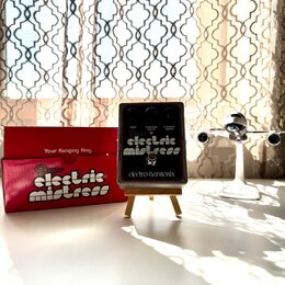 Černý efekt pedál s nápisy RATE, FLANGER DEPTH a CHORUS DEPTH u ovládacích knoflíků. Uprostřed je bílý nápis electric mistress a v dolní části značka…