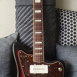 Elektrická kytara s trupem v barevném přechodu od žluté přes hnědou k černé a s hnědým hmatníkem. Na hlavě je nápis Fender, na krytu snímačů je nápis…