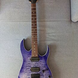 Elektrická kytara s modrým průsvitným povrchem s výraznou strukturou dřeva. Na hlavě hmatníku je viditelné logo Ibanez. Nástroj má dva humbuckery, je…
