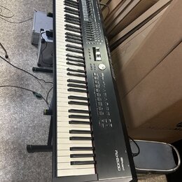 Černý digitální klavír na černém stojanu. Na pravé straně korpusu je bílý nápis „Roland RD-2000“. Nástroj vykazuje běžné známky používání a je umístě…