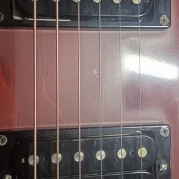 Detail korpusu červené elektrické kytary s dvěma černými humbuckery. Na spodním snímači je bílý nápis Seymour Duncan. Povrch laku vykazuje drobné škr…