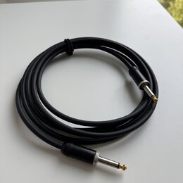Černý instrumentální kabel s konektory typu jack. Konektory mají stříbrné kovové části a zlaté hroty. Kabel je svinutý do kruhu a upevněný černým sta…