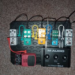 Na černém efektovém pedalboardu je umístěno šest kytarových pedálů a jedno audio rozhraní. Zleva doprava jsou řazeny pedály s nápisy AD-6, VALETON TU…
