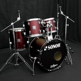 Tmavě červená bicí souprava s chromovaným hardwarem. Na přední straně basového bubnu je bílý nápis SONOR a logo Zildjian. Na ostatních bubnech jsou v…