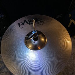 Kruhový činel z lehce žlutého kovu s koncentrickými rýhami na povrchu. Na povrchu je černý nápis Paiste 2002 a pod ním text 16" HI-HAT TOP. Činel je…