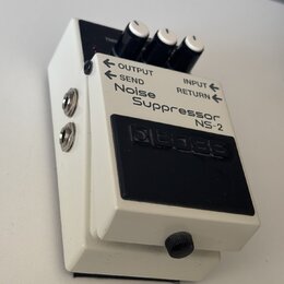 Bílý efekt pedál s černým spínacím tlačítkem, na kterém je vyražen nápis BOSS. Na horní části jsou tři ovládací knoflíky a nápisy OUTPUT, INPUT, SEND…