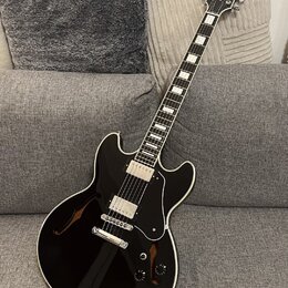 Černá polodublová elektrická kytara s bílým lemováním a černým pickguardem. Na hlavě hmatníku je viditelné logo Gibson. Nástroj má dva humbuckery, čt…
