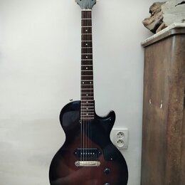 Elektrická kytara s tmavě hnědým gradientem (sunburst) a černým hmatníkem. Na hlavě je bílý nápis Epiphone. Nástroj má dva humbuckery, jeden tónový a…