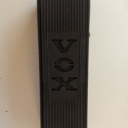 Černý obdélníkový pedál s povrchem z rýhované gumy. Uprostřed je vyryto logo VOX a nápisy AMPLIFIER a INSTRUMENTS. Povrch vykazuje mírné známky opotř…