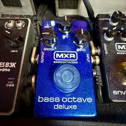 Modrý efekt pedál s kovovým povrchem a třemi ovládacími knoflíky. Na přední straně je bílé logo MXR a nápis BASSINNOVATIONS, dále popisky MID+, GROWL…
